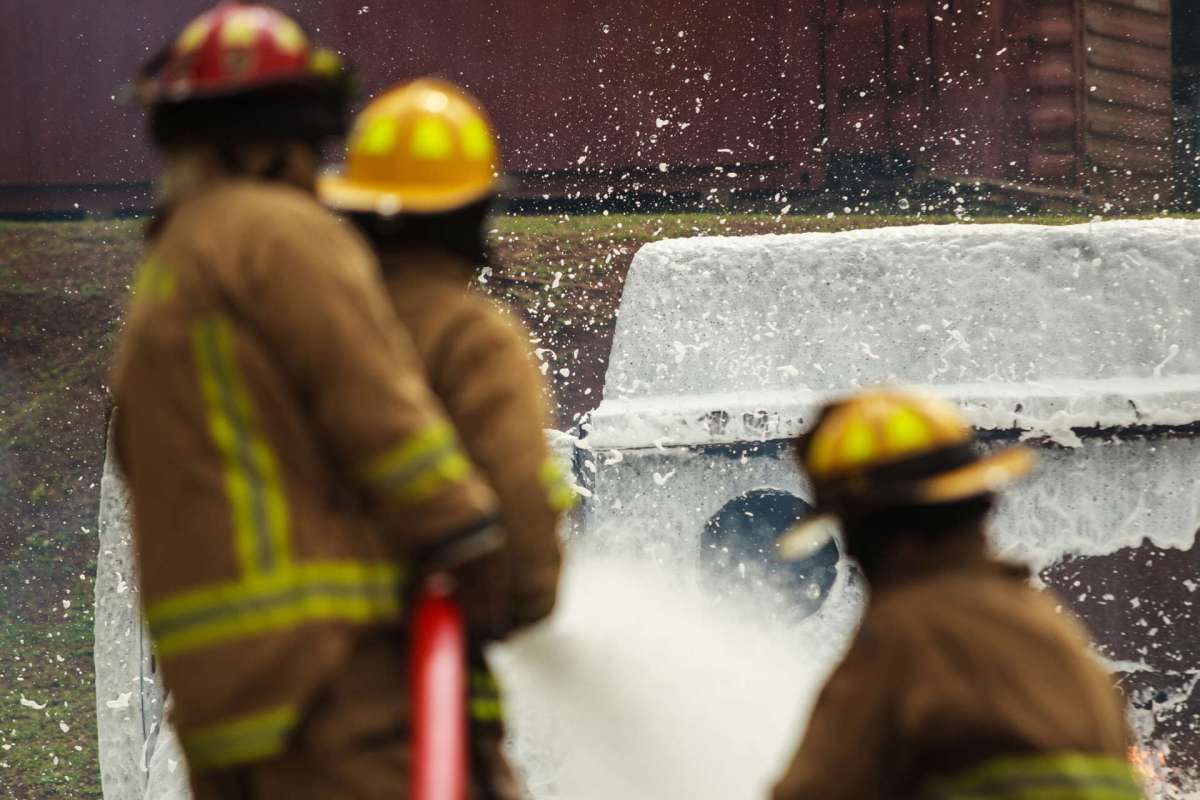 Firefighters spray foam on a vehicle during a training exercise.