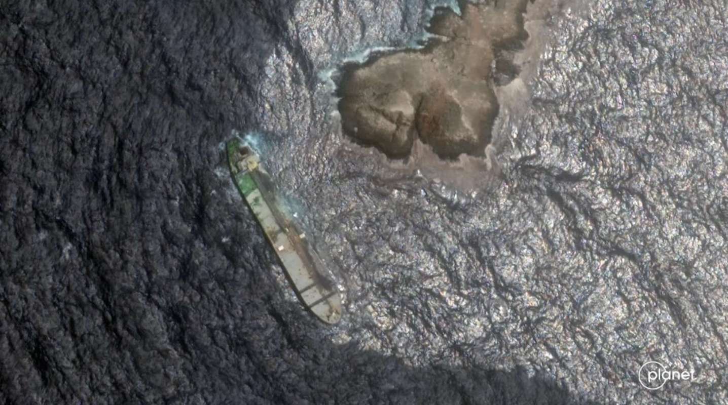 A cargo ship near a rocky island surrounded by water.