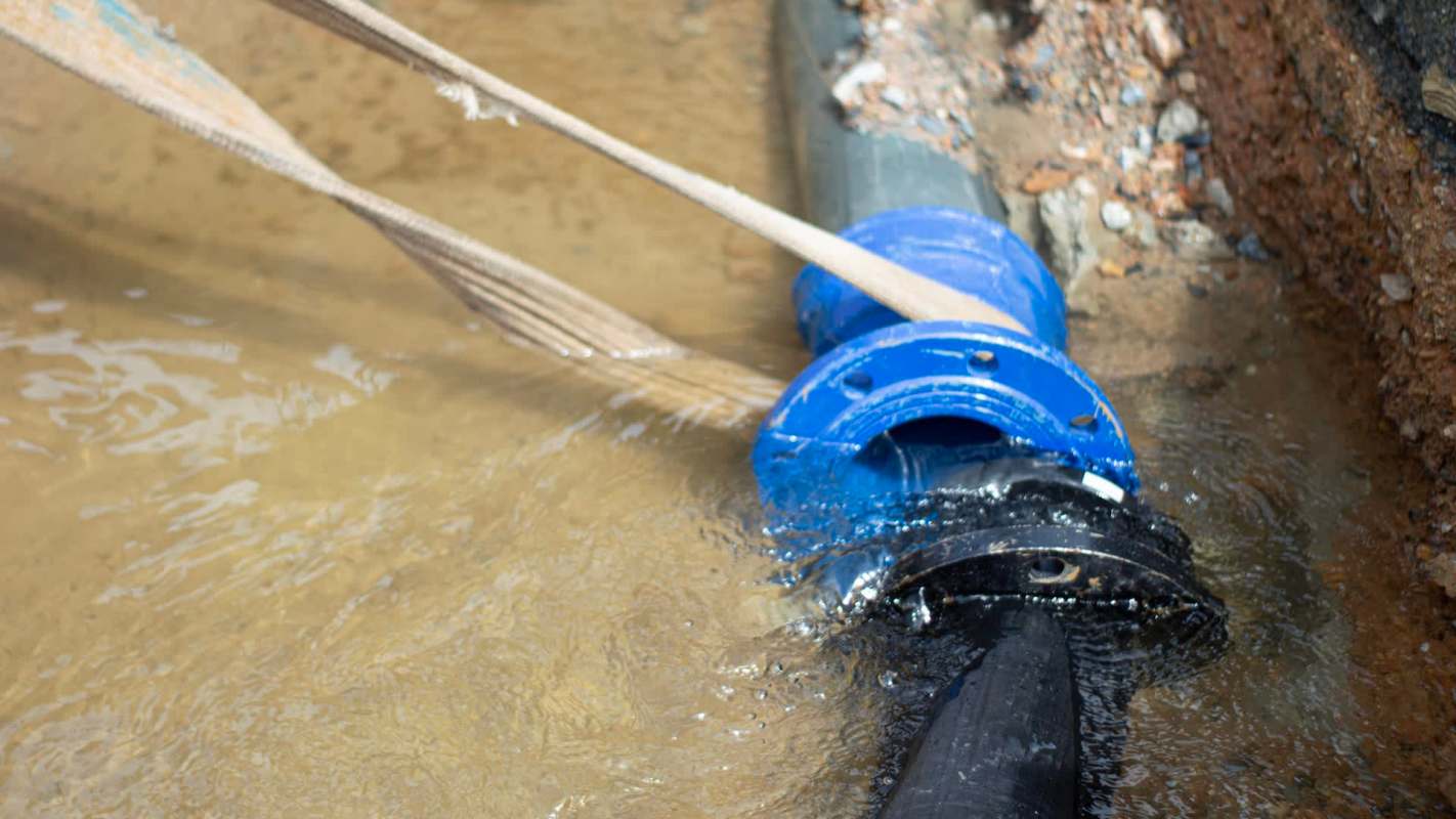 A blue water pipe connected to a dark pipe in muddy water at a construction site.