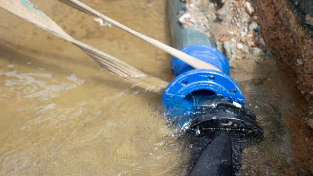 A blue water pipe connected to a dark pipe in muddy water at a construction site.