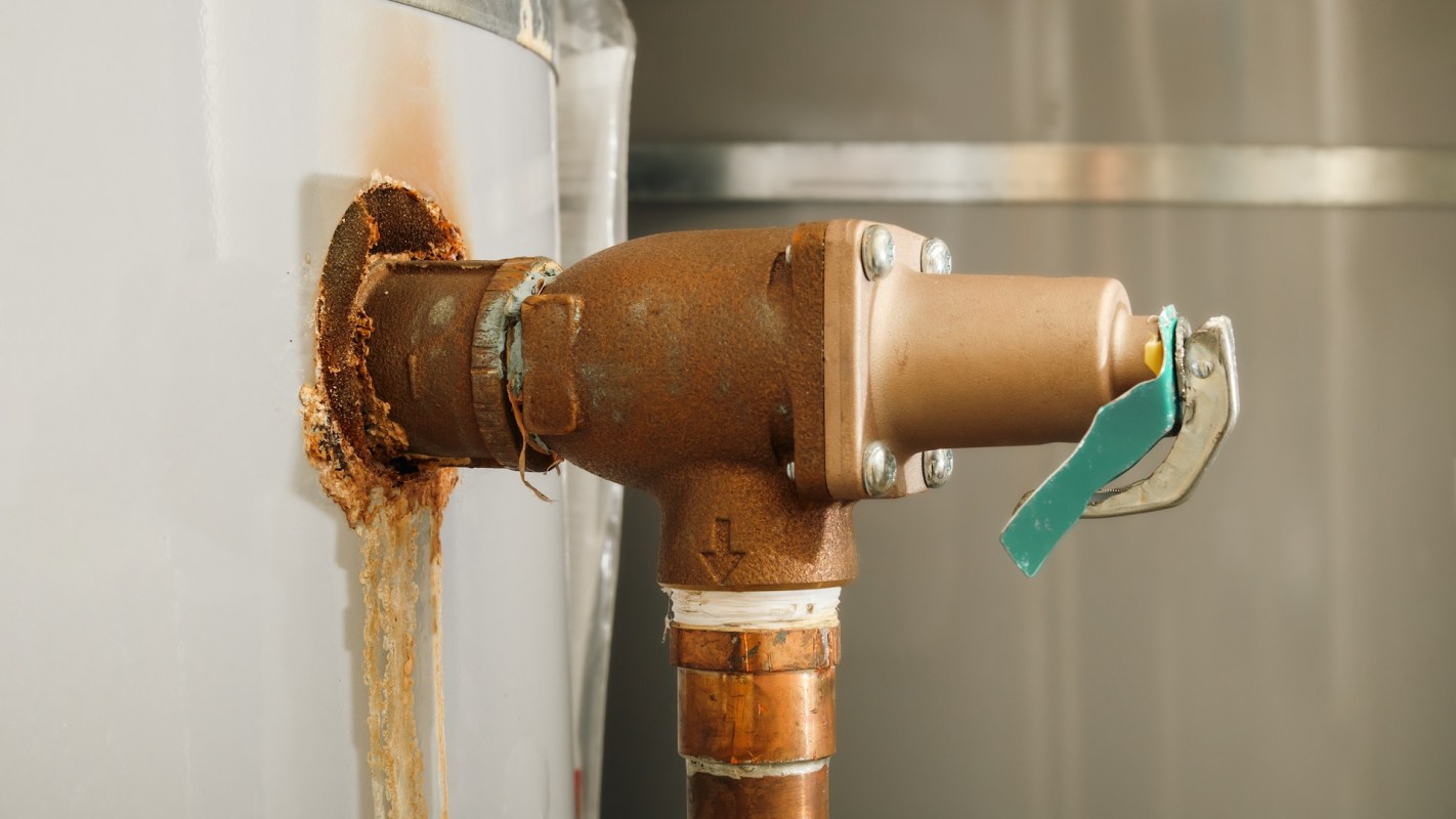 A rusty pipe connected to a water heater with water leaking from the joint.