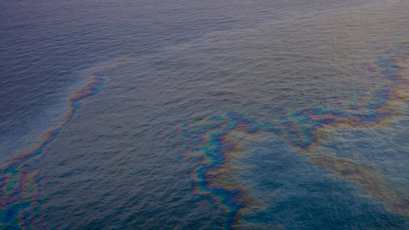An oil spill creates a rainbow sheen on the surface of the water.
