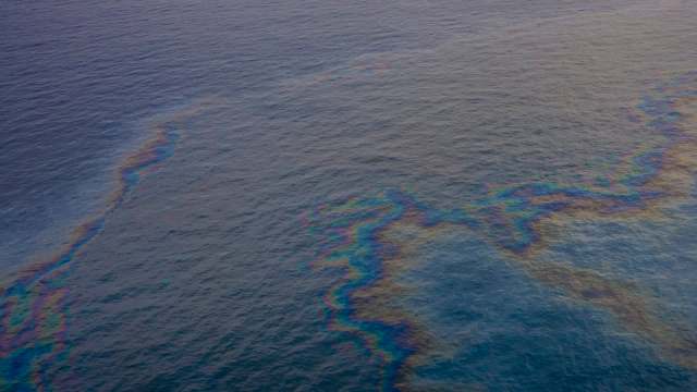An oil spill creates a rainbow sheen on the surface of the water.