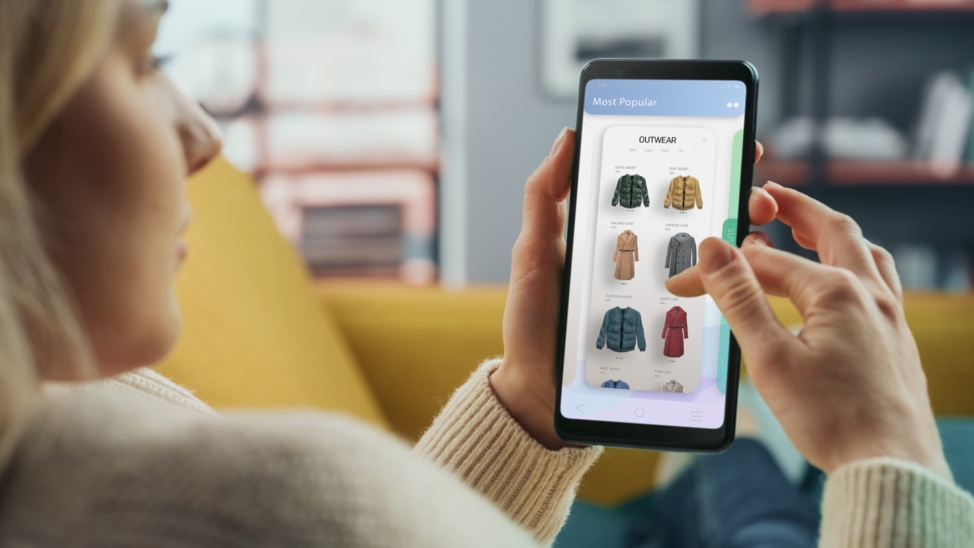 A person using a smartphone to browse a clothing shopping app displaying various jackets.