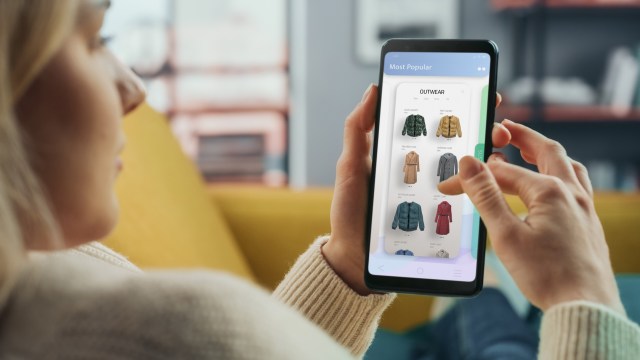 A person using a smartphone to browse a clothing shopping app displaying various jackets.