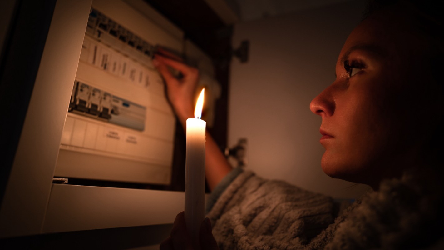 A person holds a candle while interacting with a circuit breaker box in a dimly lit environment.