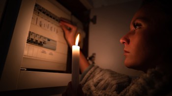 A person holds a candle while interacting with a circuit breaker box in a dimly lit environment.