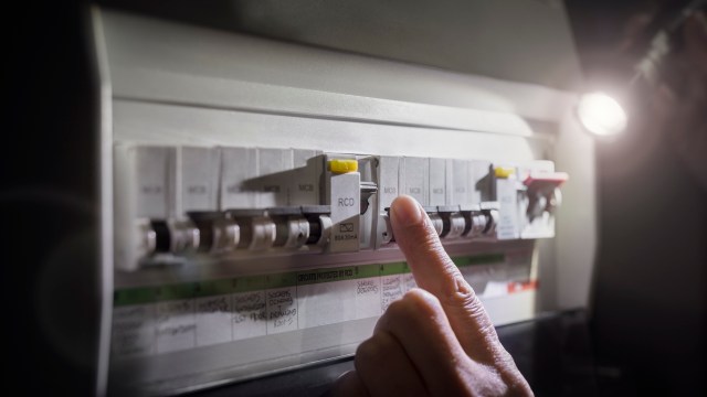 A finger is pressing a switch on a circuit breaker panel.
