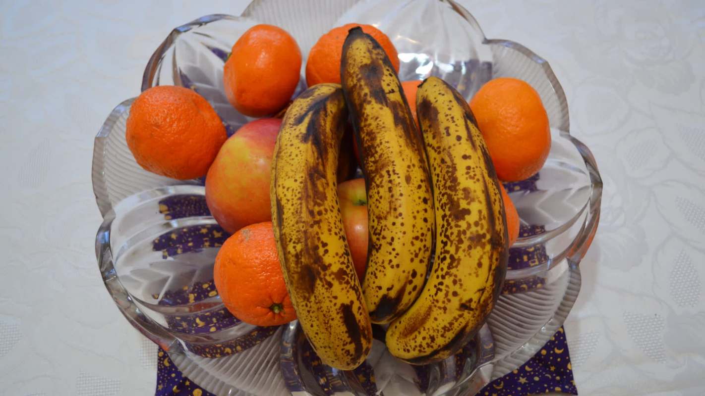 A bowl of bananas, oranges, and apples on a patterned surface.