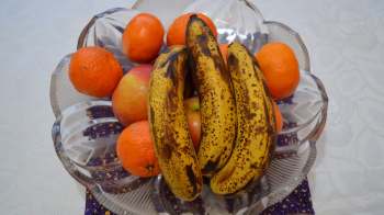 A bowl of bananas, oranges, and apples on a patterned surface.