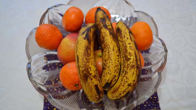 A bowl of bananas, oranges, and apples on a patterned surface.