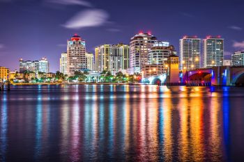 City skyline with lit buildings and a bridge reflected in the water at night.