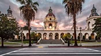 A city hall building with a dome and arched entrance, framed by palm trees and a cloudy sky.