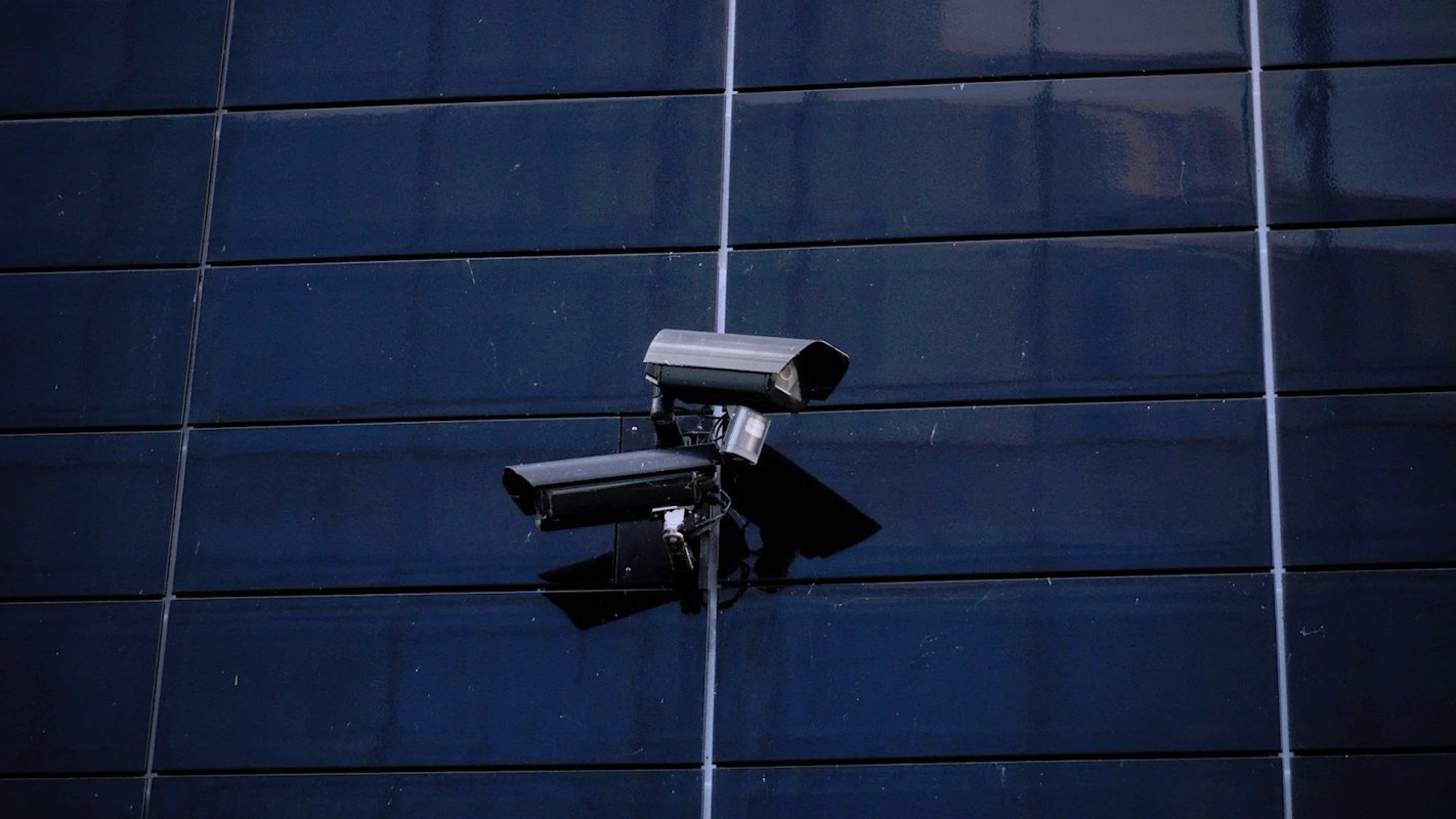 Two security cameras mounted on a dark, reflective building surface.