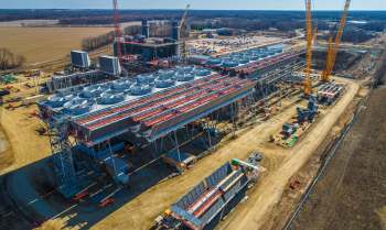 A large industrial facility under construction with cooling towers and cranes in a partially developed area.