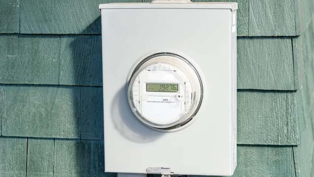 An electric meter mounted on a wall with green shingles.