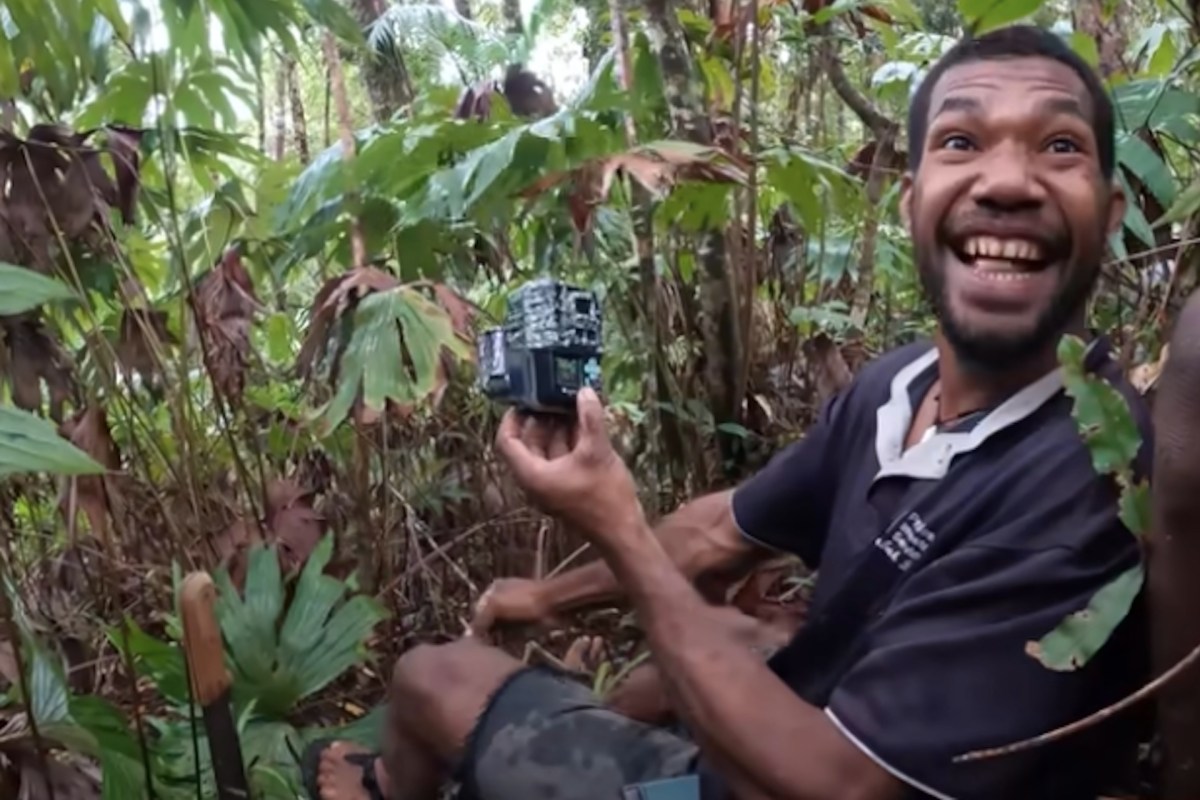 A man showcasing a hidden camera in a tropical forest.