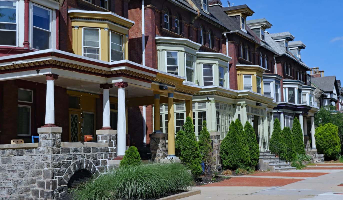 Row of Victorian-style houses with colorful bay windows and landscaped front yards.