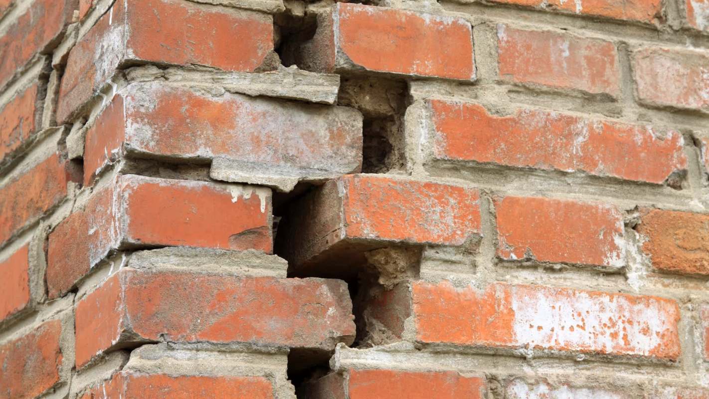 A close-up of a brick wall showing noticeable cracks and missing mortar between the bricks.