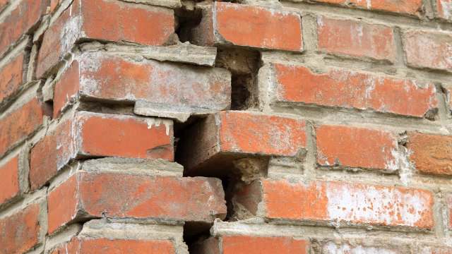 A close-up of a brick wall showing noticeable cracks and missing mortar between the bricks.