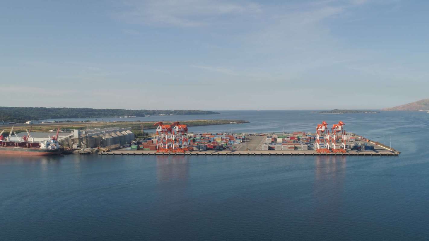 A port with cargo containers and cranes on a calm waterway.