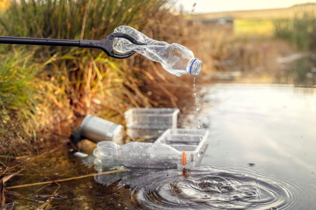 A person using a grabber to pick up plastic waste.