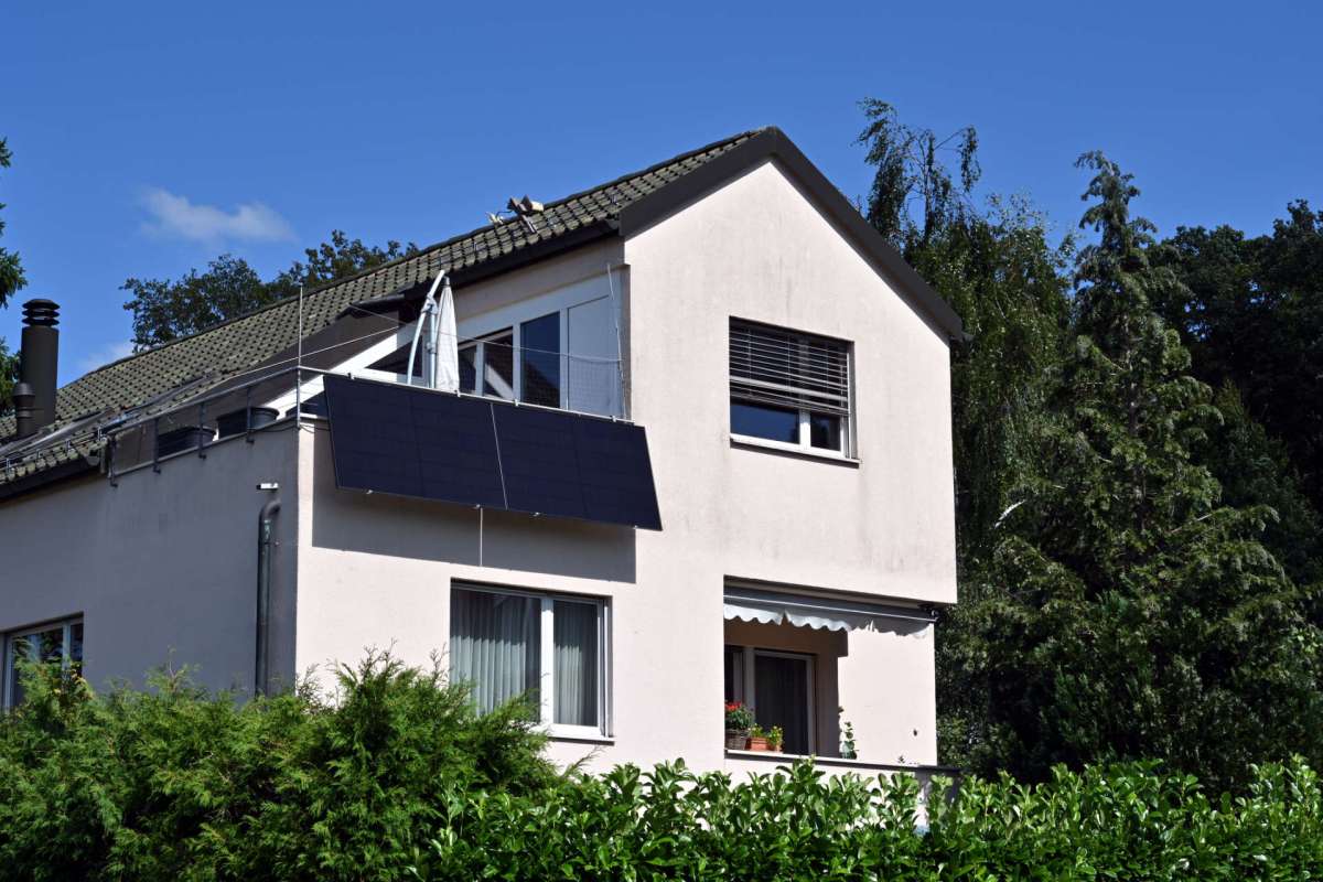 A house with solar panels, surrounded by greenery and trees, under a blue sky.