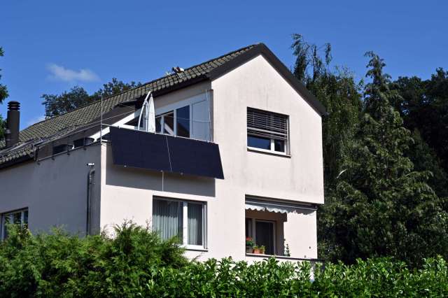 A house with solar panels, surrounded by greenery and trees, under a blue sky.