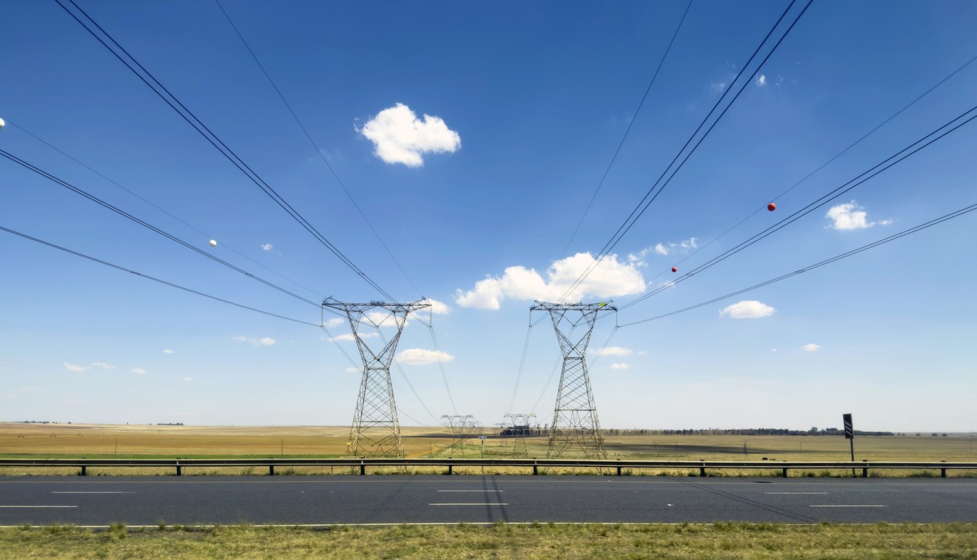Power lines stretch across an open field under a clear blue sky with a few clouds.