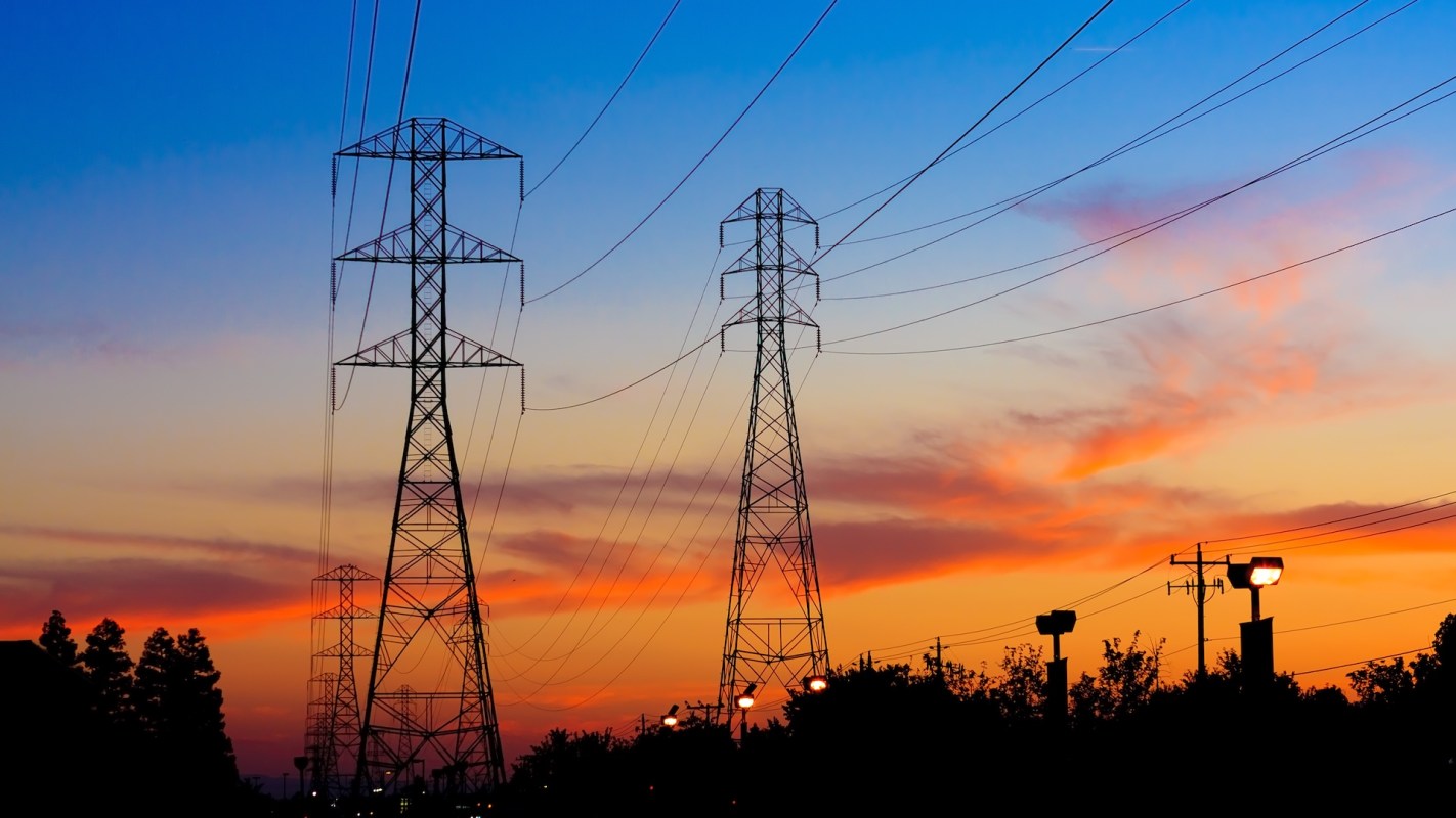 Power lines and transmission towers silhouetted against a colorful sunset sky.