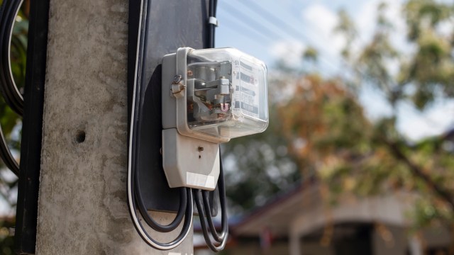 An electricity meter mounted on a concrete pole with exposed wiring.