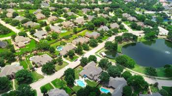 An aerial view of a suburban neighborhood with houses, trees, and a pond.