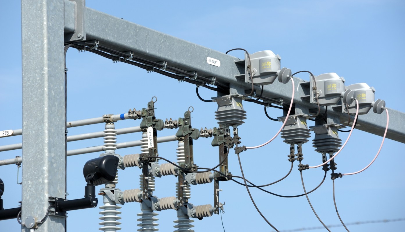 Electrical distribution equipment mounted on a metal pole against a blue sky.