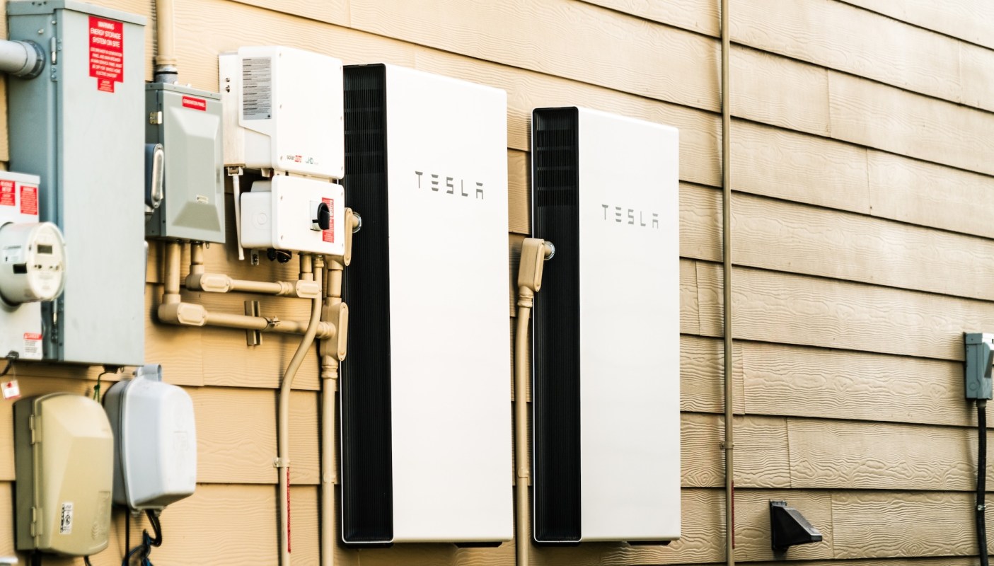 Two Tesla energy storage units mounted on a wall alongside electrical equipment and piping.