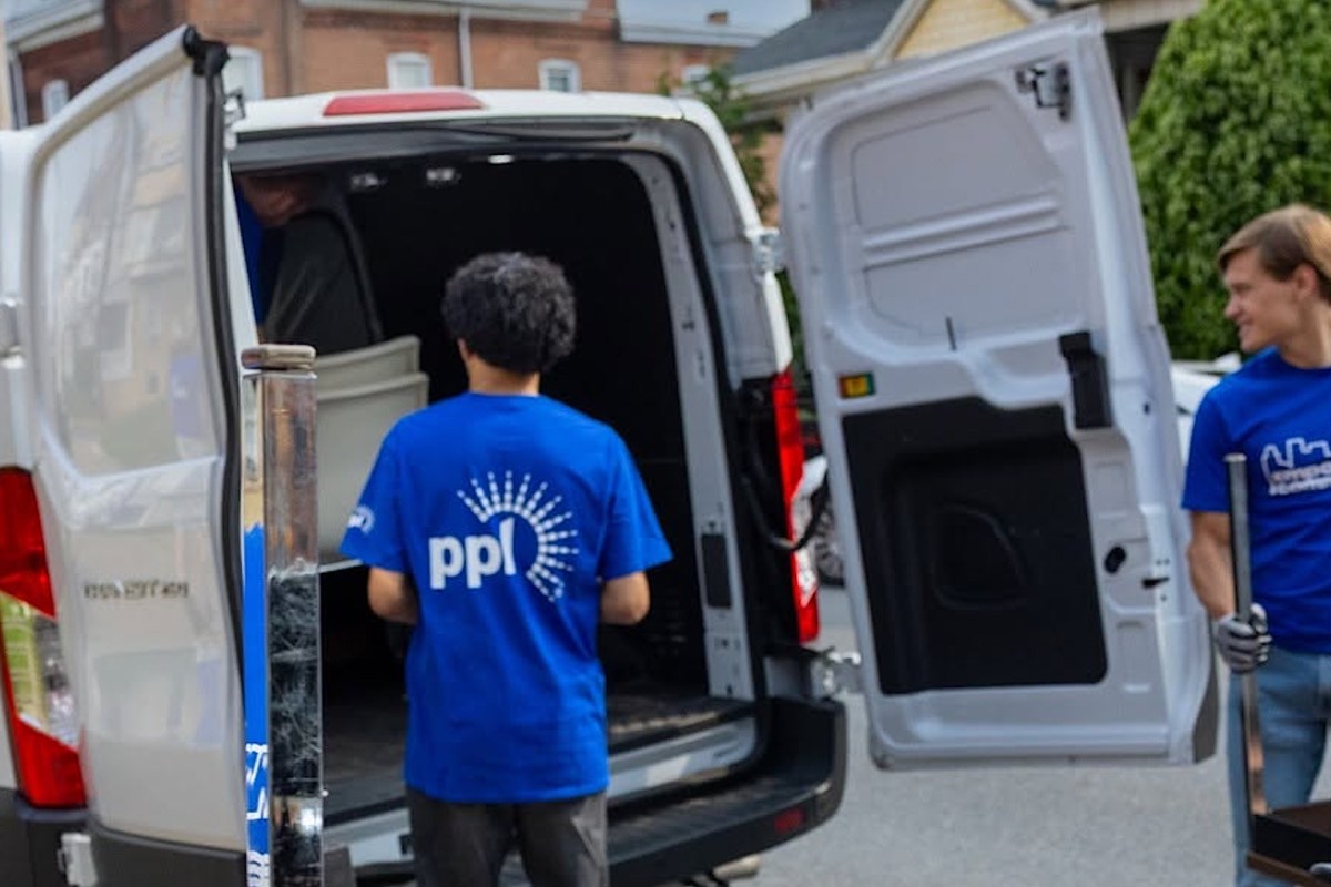 Two people are unloading items from the back of a van parked on a street.