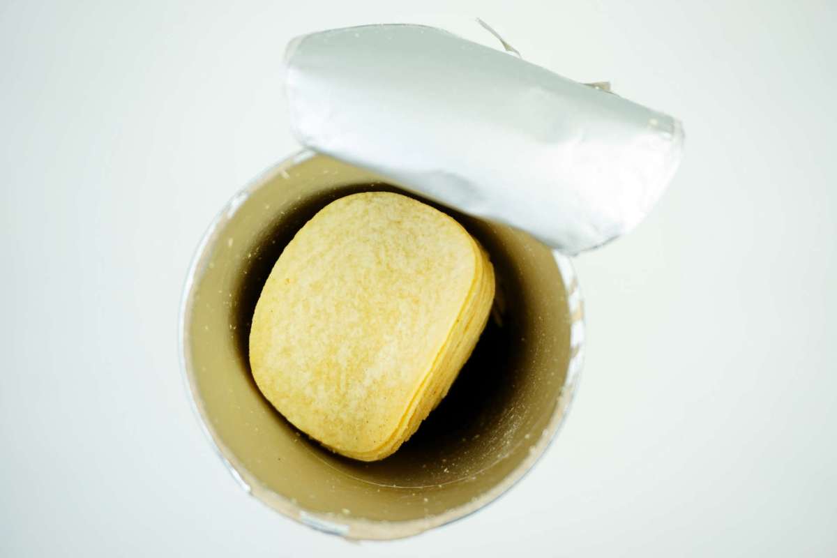 A cylindrical container with a partially removed lid and layered snacks inside.