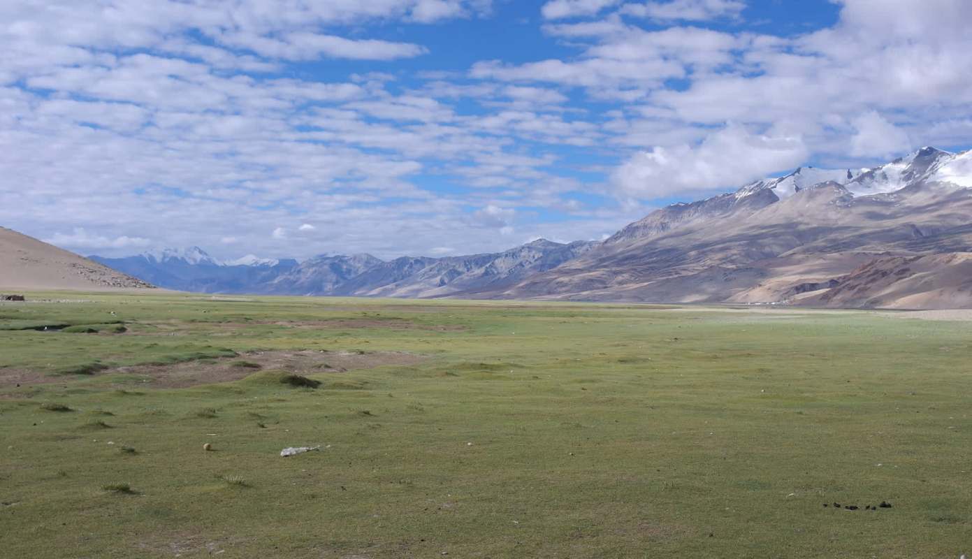 A vast landscape featuring green grass, mountains, and a partly cloudy sky.