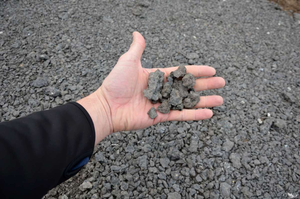 A hand holds several pieces of gray volcanic rock above a surface of gravel.