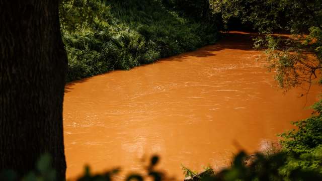 A river with orange water flowing beside lush greenery.