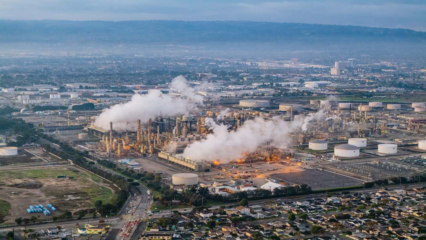 An industrial area with oil refineries, storage tanks, and smoke emissions.