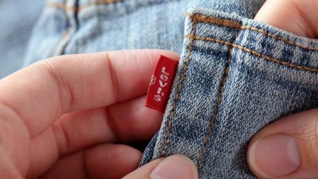 A hand holding a tag on a piece of denim clothing.