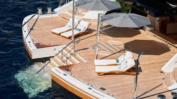 Loungers and umbrellas set on the deck of a yacht overlooking the water.