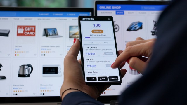 A person interacts with a rewards app on a smartphone with an online shopping website in the background.