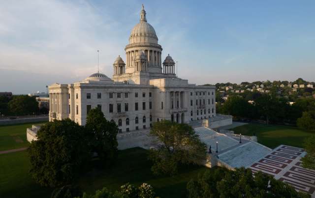 The Rhode Island State House, surrounded by green trees and lawns.