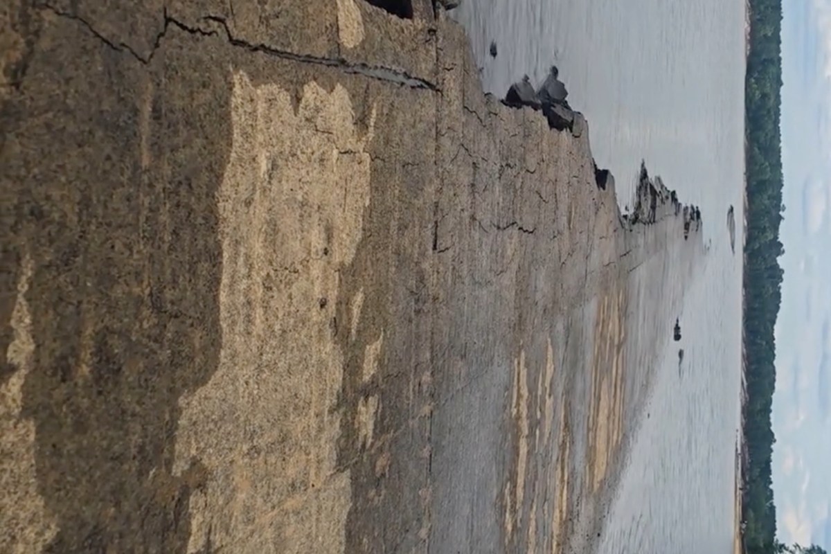 A weathered stone structure leads into a body of water with trees in the background.