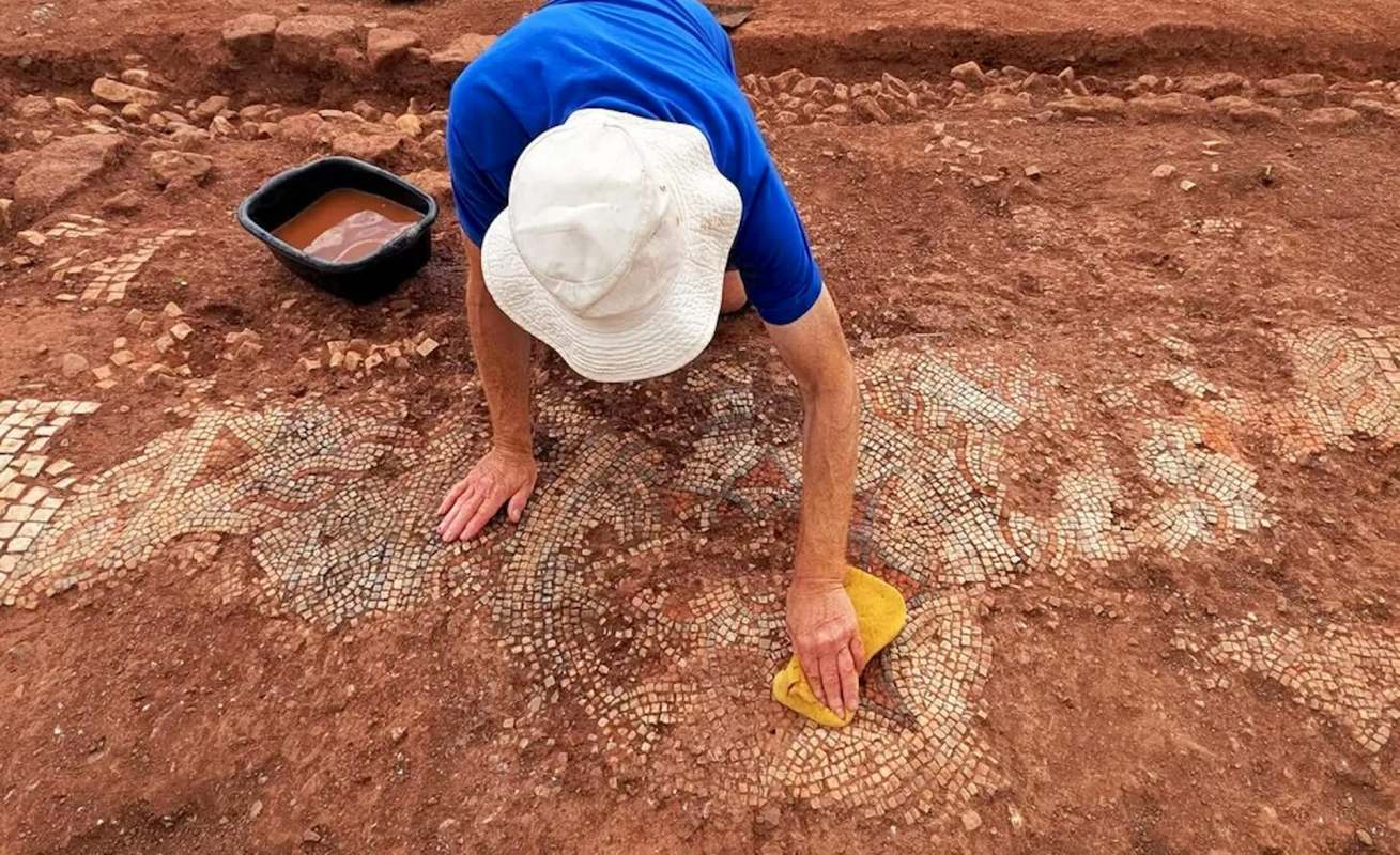 An individual cleans an ancient mosaic at an archaeological site.