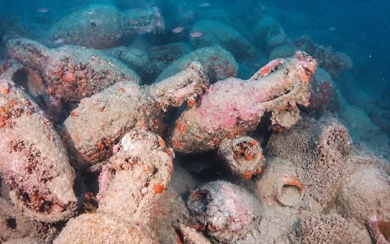 An underwater scene featuring numerous ancient amphorae covered in sand and marine life.