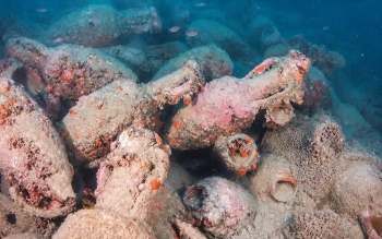 An underwater scene featuring numerous ancient amphorae covered in sand and marine life.
