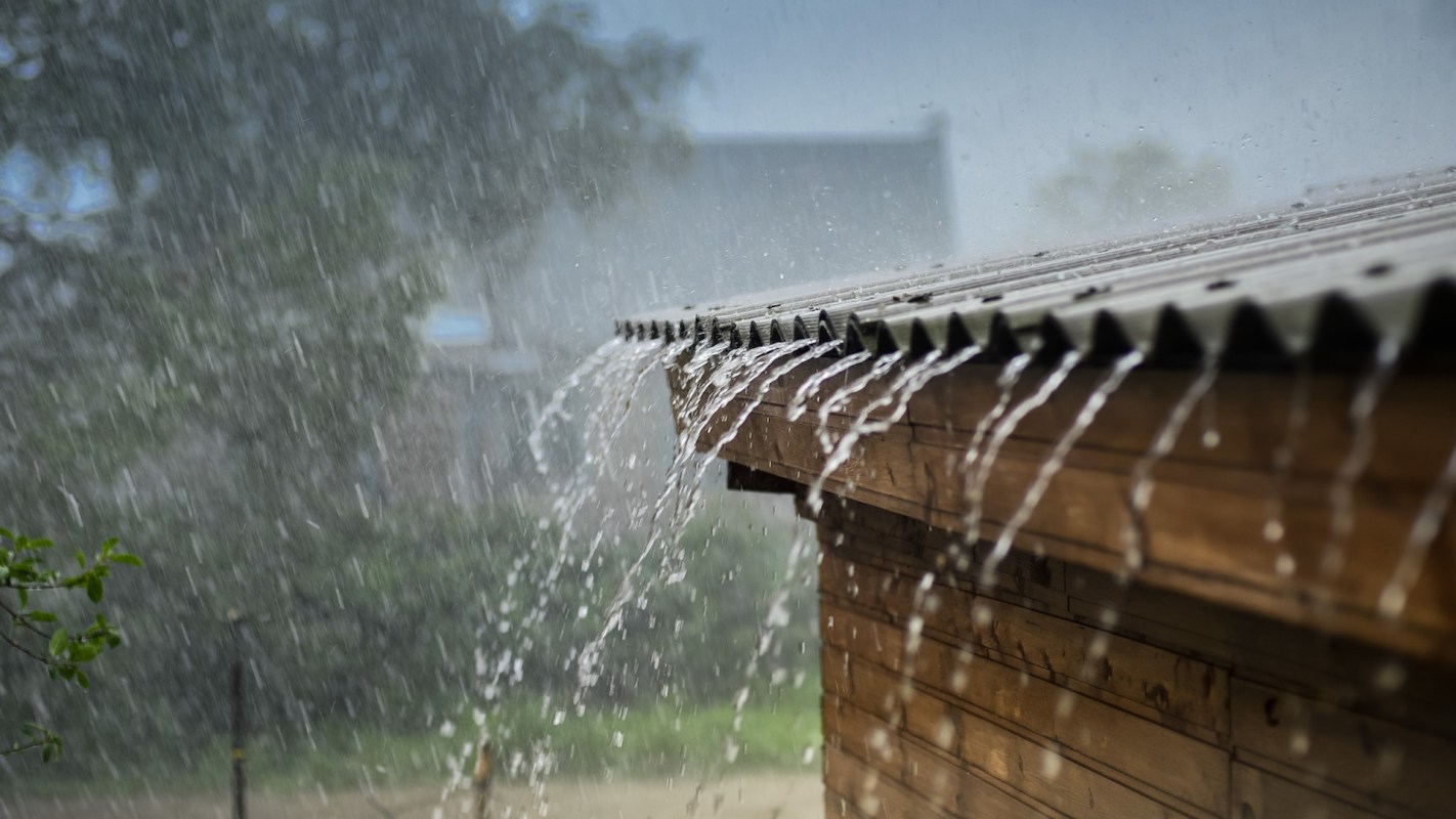 Rainwater pours off a roof into an outdoor area during a heavy rainstorm.