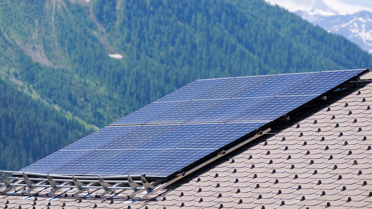 Solar panels installed on a sloped roof with green mountains in the background.